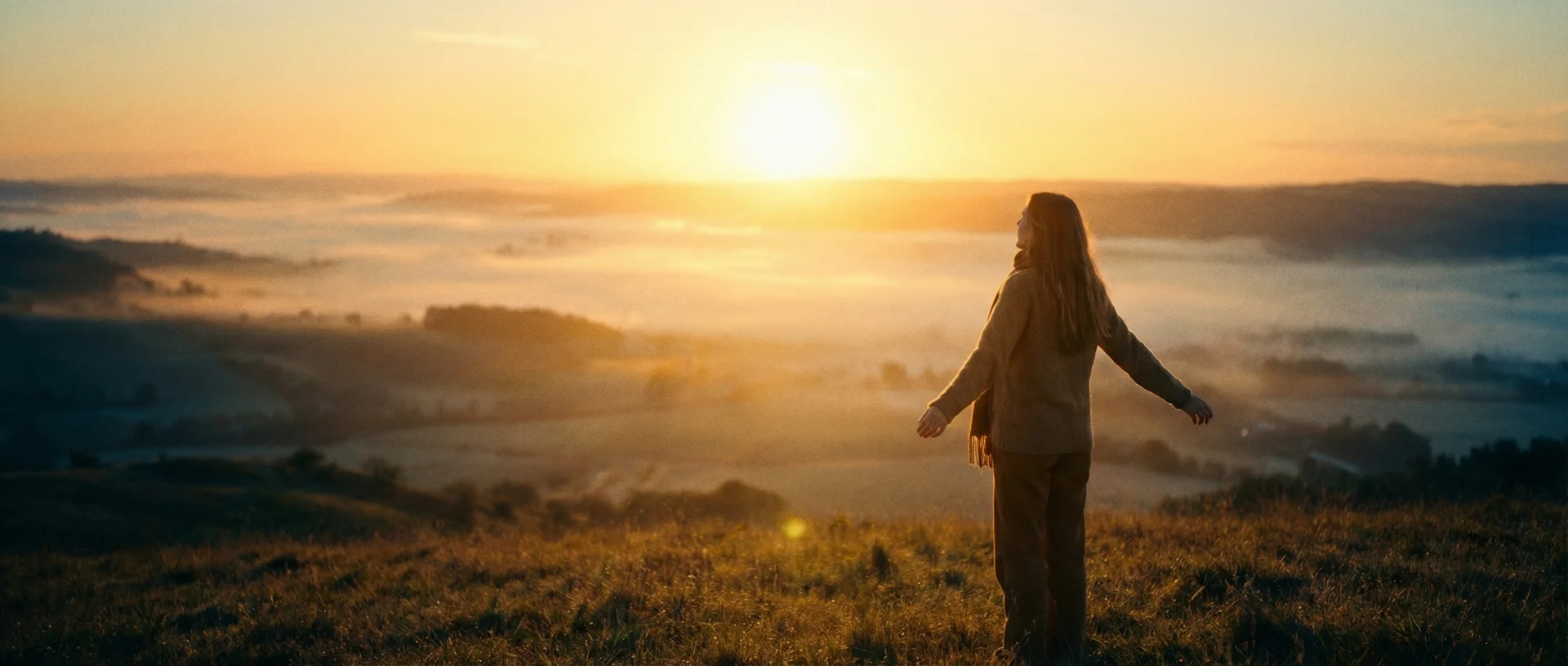 Frau steht bei Sonnenaufgang auf einem Hügel mit ausgebreiteten Armen - Symbol für innere Freiheit und Klarheit